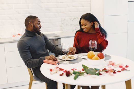 Couple souriant lors d'un dîner romantique, assis à une table décorée de pétales de rose et de fruits.